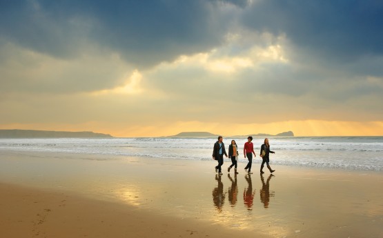 Four students walking across Rhosilli beach, with Worms head in the distance