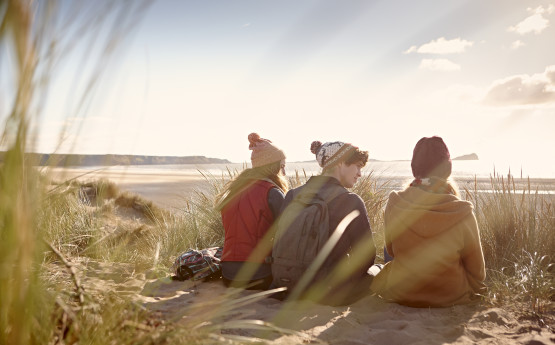 Three students sitting on the dunes at Bay campus looking out over the sea