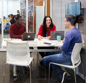 Three students chatting at a desk in a private study room
