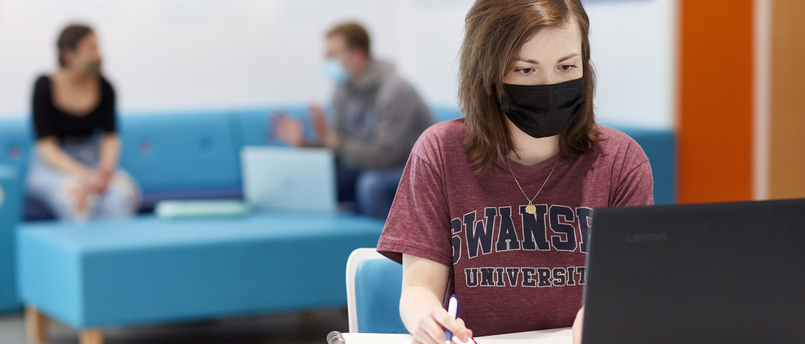 female student working at laptop in mask