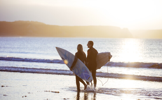 two students walking with surfboards on the beach