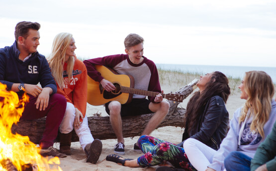 students sitting around a fire playing guitar on the beach