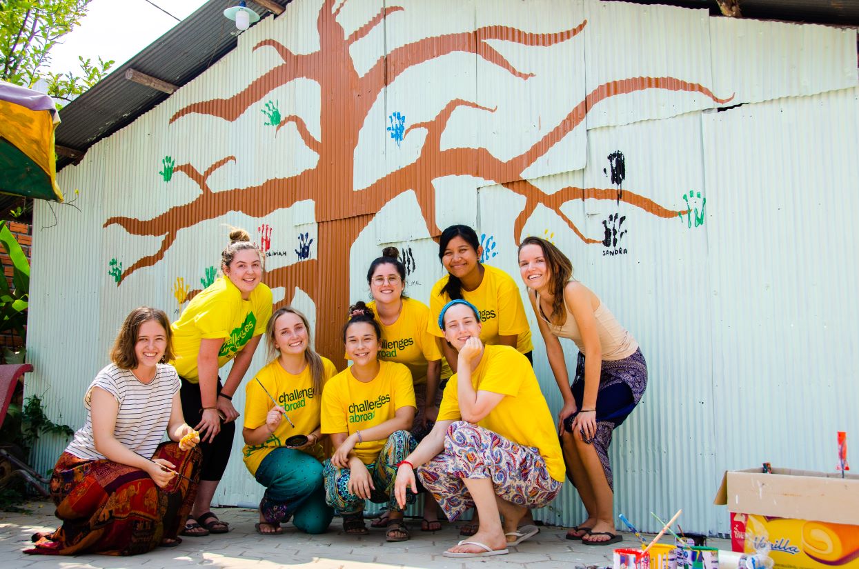 students in Cambodia in front of mural depicting a tree