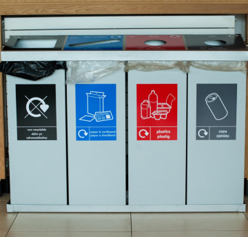 A quad recycling bin on campus which has compartments for non-recyclable waste, paper, plastic and cans