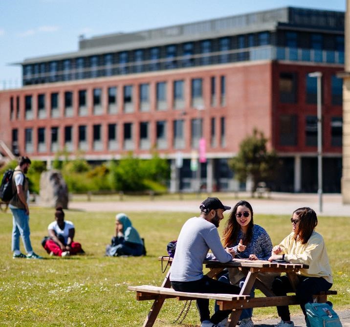 Students sitting outside the School of Management on the Bay Campus of Swansea University.