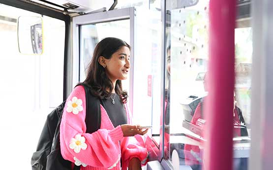 A female student wearing bright cardigan paying the driver on a First Bus
