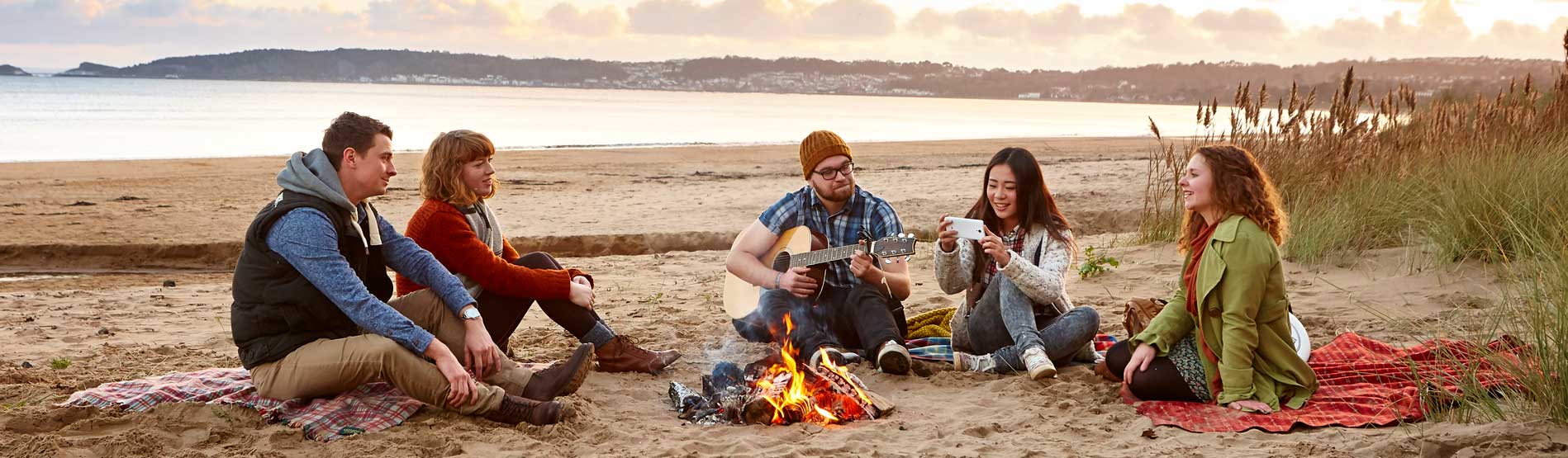 a group of students sitting round a camp fire on a gower beach