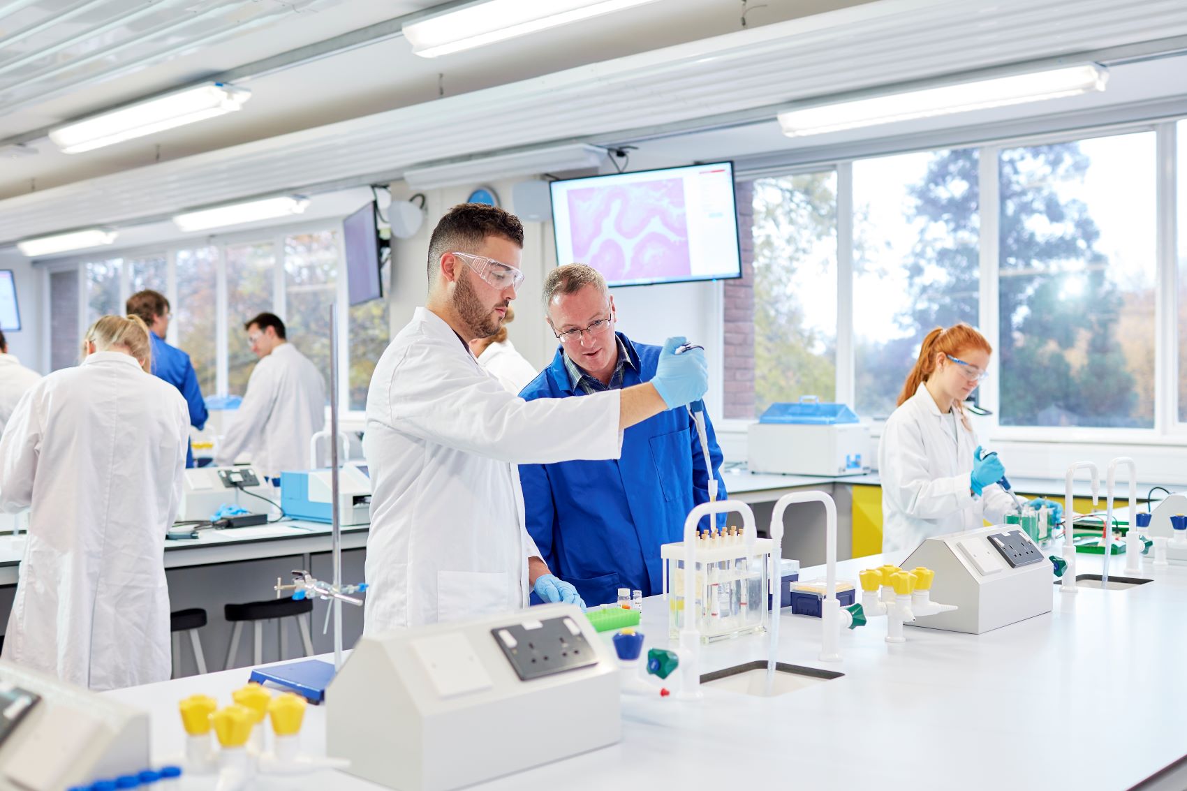 Students in white coats using pipettes in a biomedical sciences laboratory