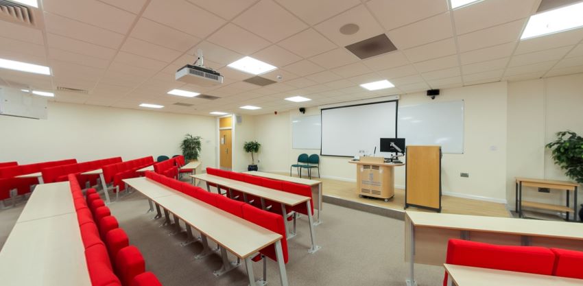 Lecture theatre with tiered red seating, podium and presentation screen
