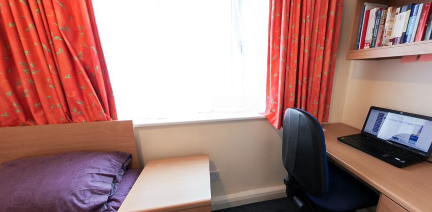 Student bedroom with bed, study desk, laptop and window with red curtains