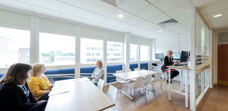 Collaborative learning space with tables, computers and seated staff