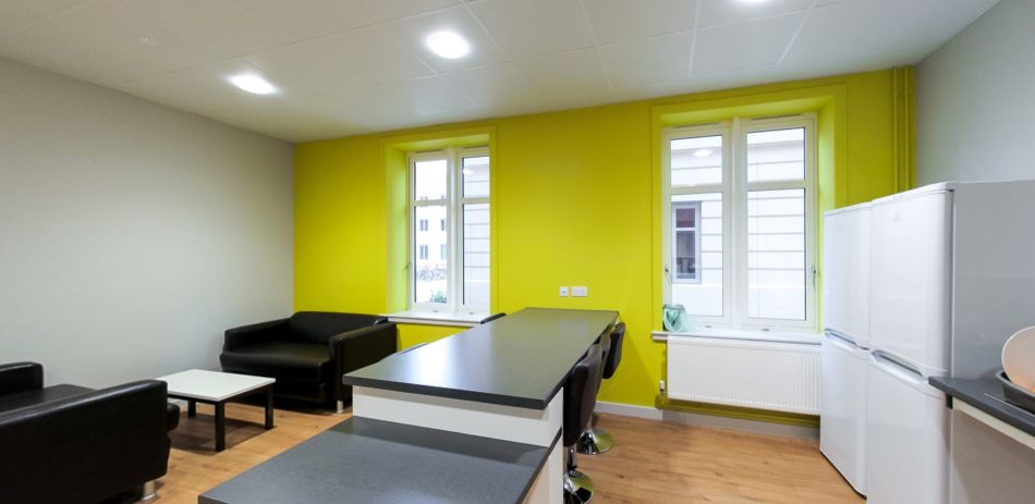 Student kitchen with breakfast bar, stools, sofa, fridge and bright window