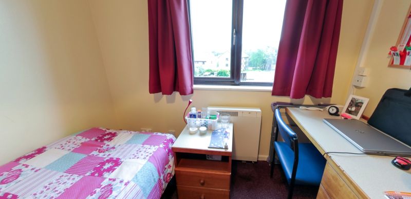 Single student bedroom with bed, desk, chair and window with red curtains