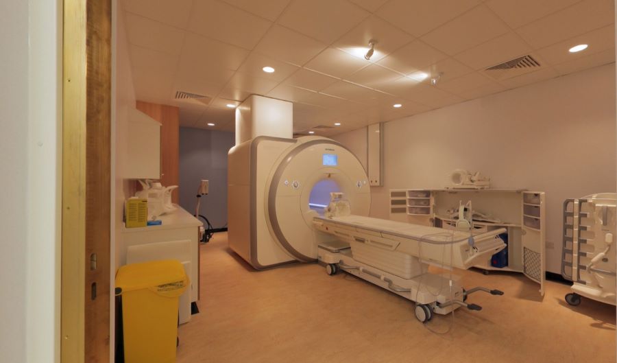 MRI scanner room with imaging machine, patient table, and medical equipment