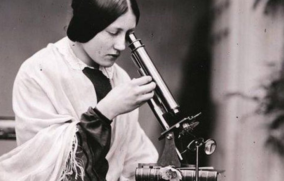 Black and white image of woman looking down microscope