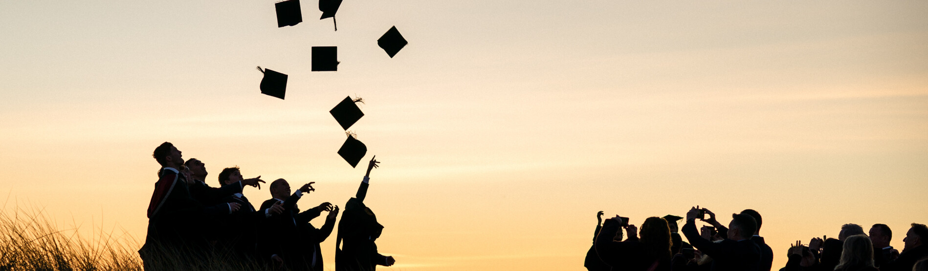 Image of students graduating, throwing hats up in the air on the beach.